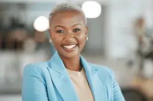 A confident woman with a short haircut, wearing a bright blue blazer, smiling at the camera in an office setting.